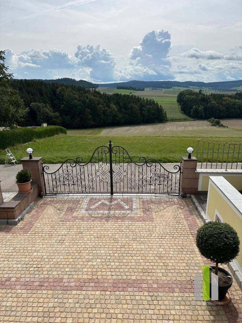 Gepflasterter Hof mit schmiedeeisernem Tor und weitem Blick über die Landschaft.