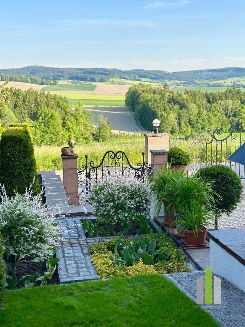 Gepflegter Gartenbereich mit schmiedeeisernem Tor und weitem Blick über die grüne Landschaft.