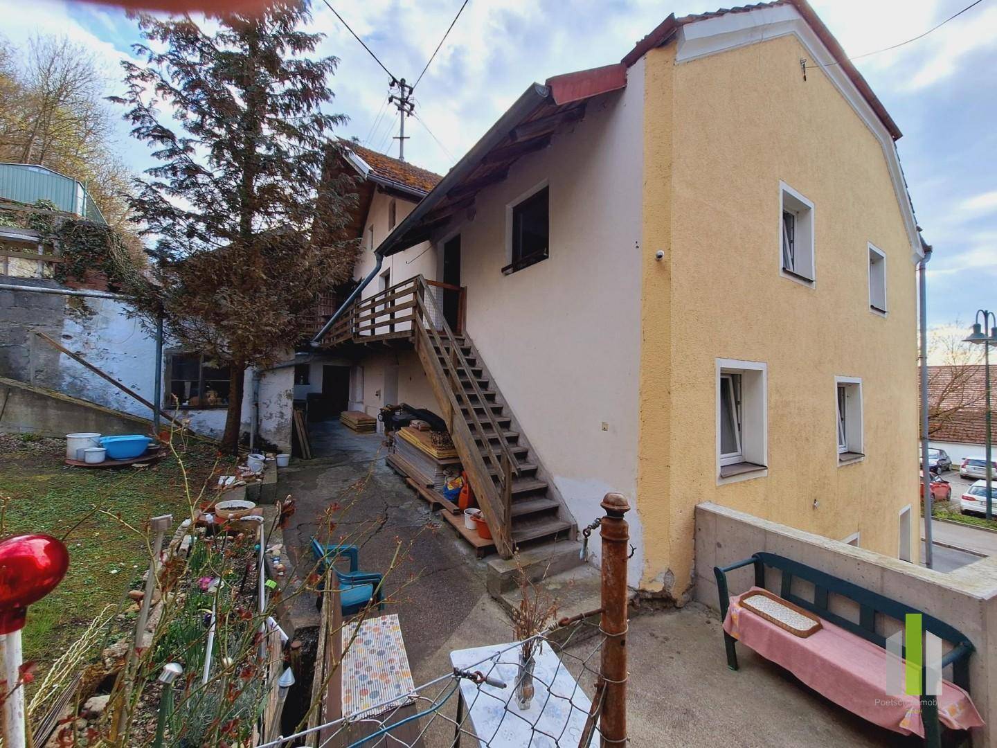 Hinterhofbereich mit hölzerner Außentreppe, kleinem Garten und einer Sitzbank.