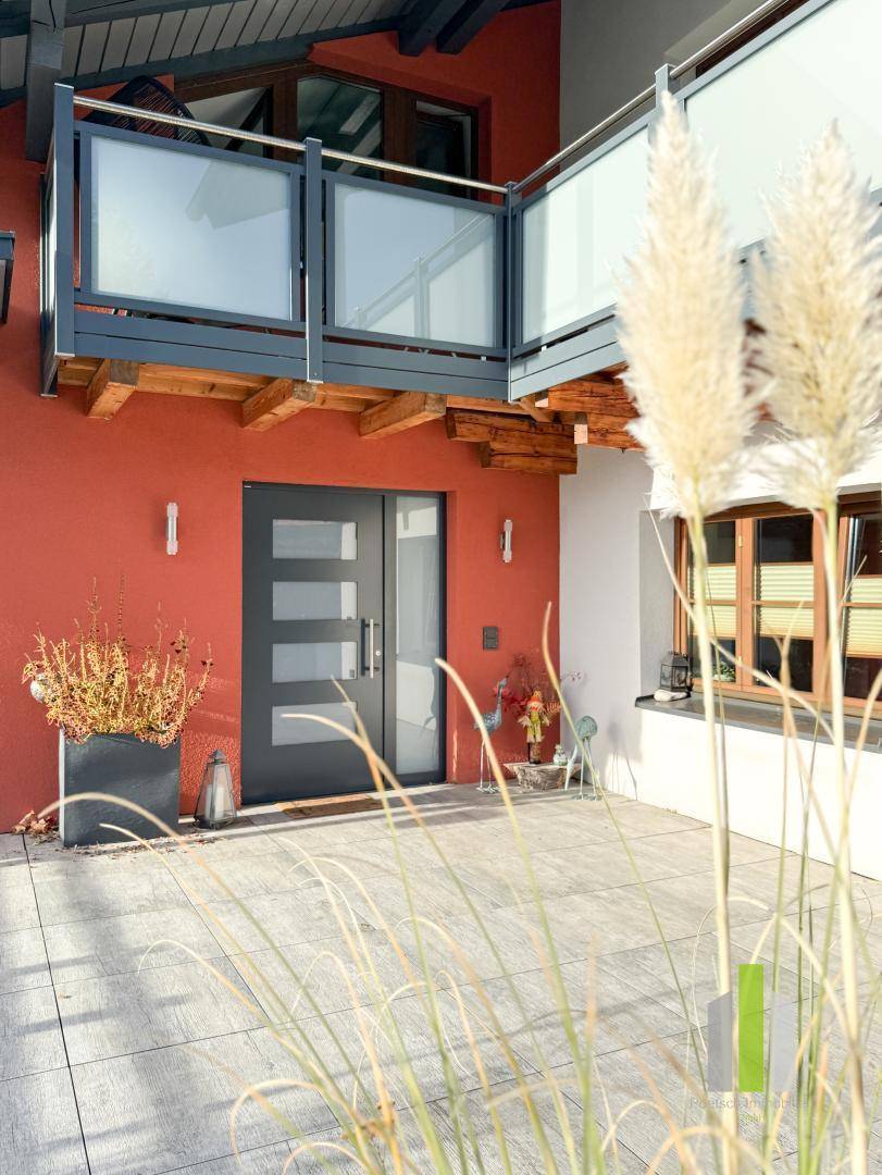 Moderner Hauseingang mit dunkler Tür, umgeben von einer hellen Terrasse und einem Balkon.