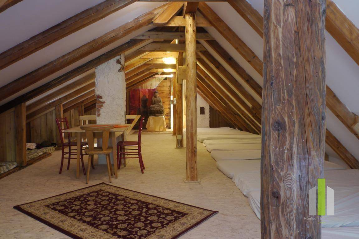Dachboden mit sichtbaren Holzbalken, Matratzen als Schlafgelegenheiten und einem kleinen Tischbereich.