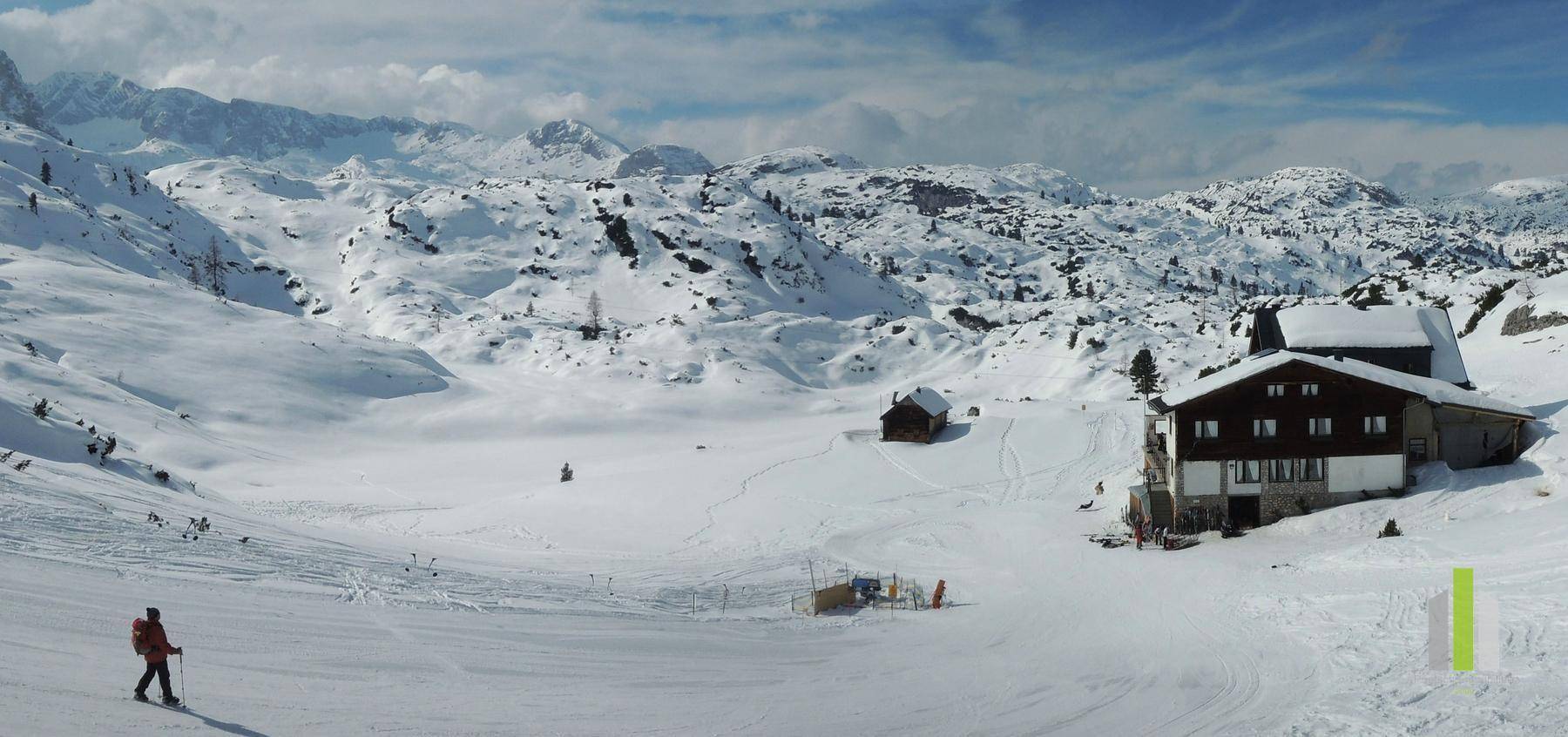 Winterliche Berglandschaft mit schneebedeckten Hängen und einer Berghütte im Tal.