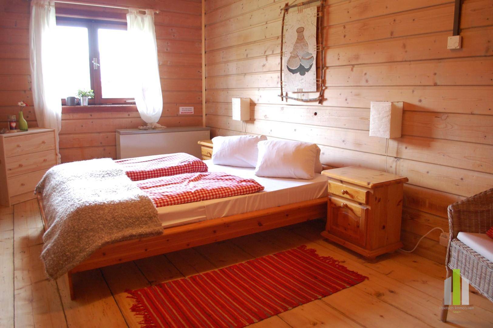 Gemütliches Schlafzimmer mit Holzwänden, Doppelbett und einem Fenster, das viel Licht hereinlässt.