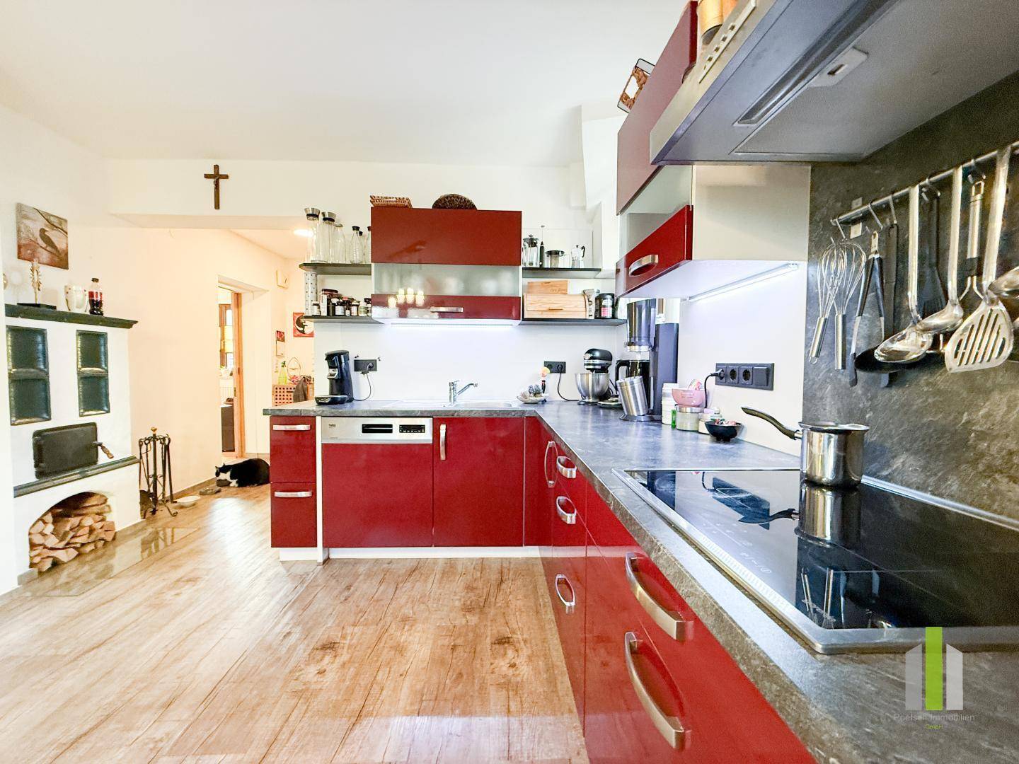 Moderne Einbauküche mit glänzenden roten Fronten, dunklen Arbeitsplatten und Holzboden.