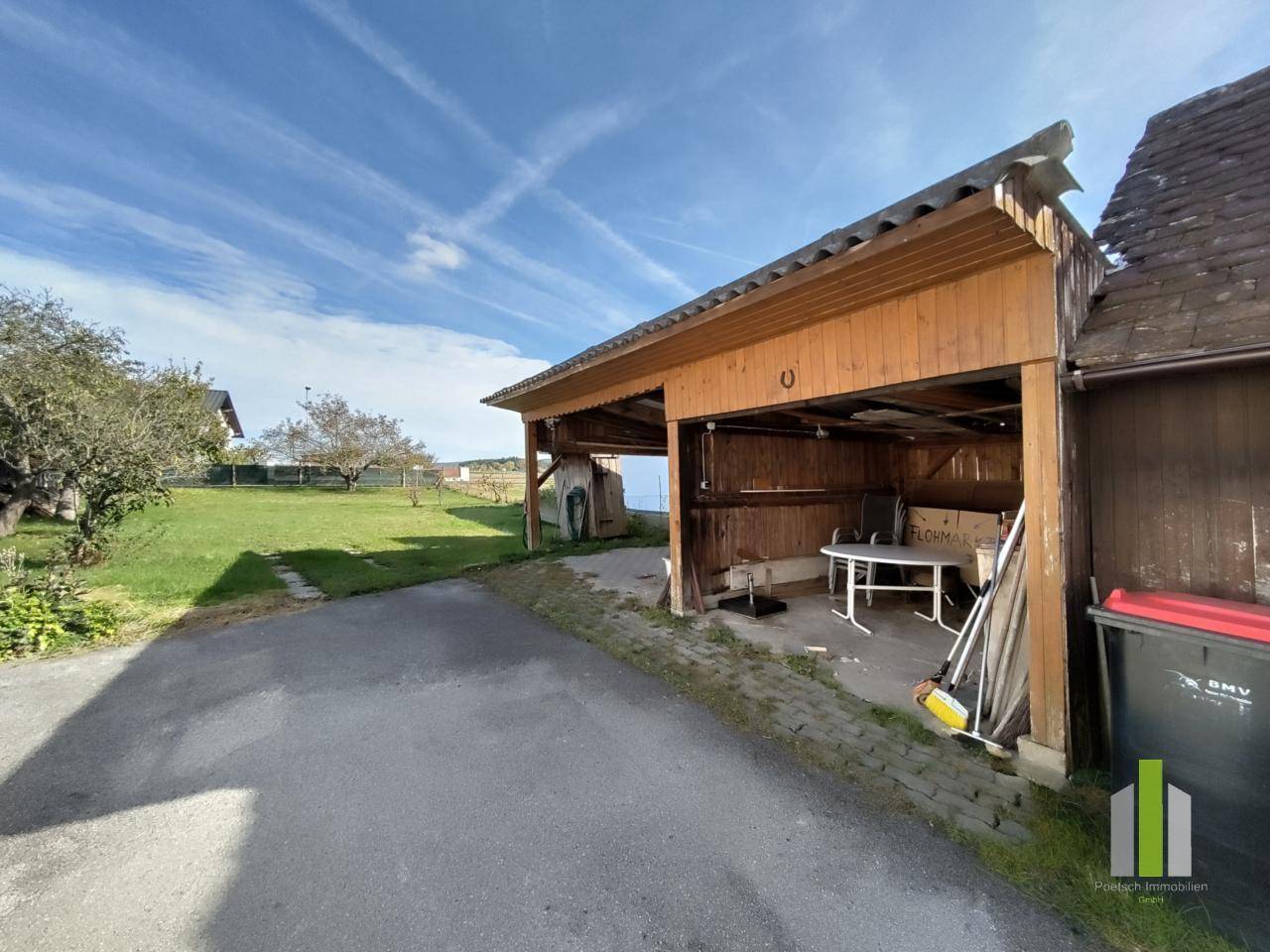 Überdachter Carport aus Holz mit Abstellfläche und Blick auf den weitläufigen Garten.