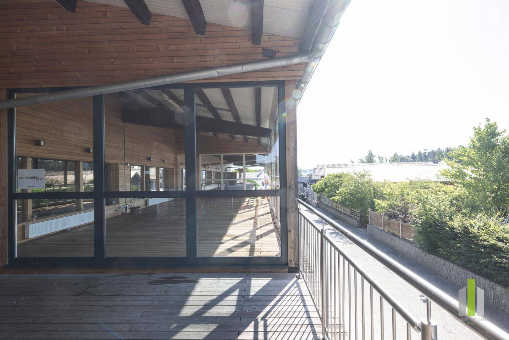 Großer Holzbalkon mit Metallgeländer und Blick auf die Umgebung an einem sonnigen Tag.