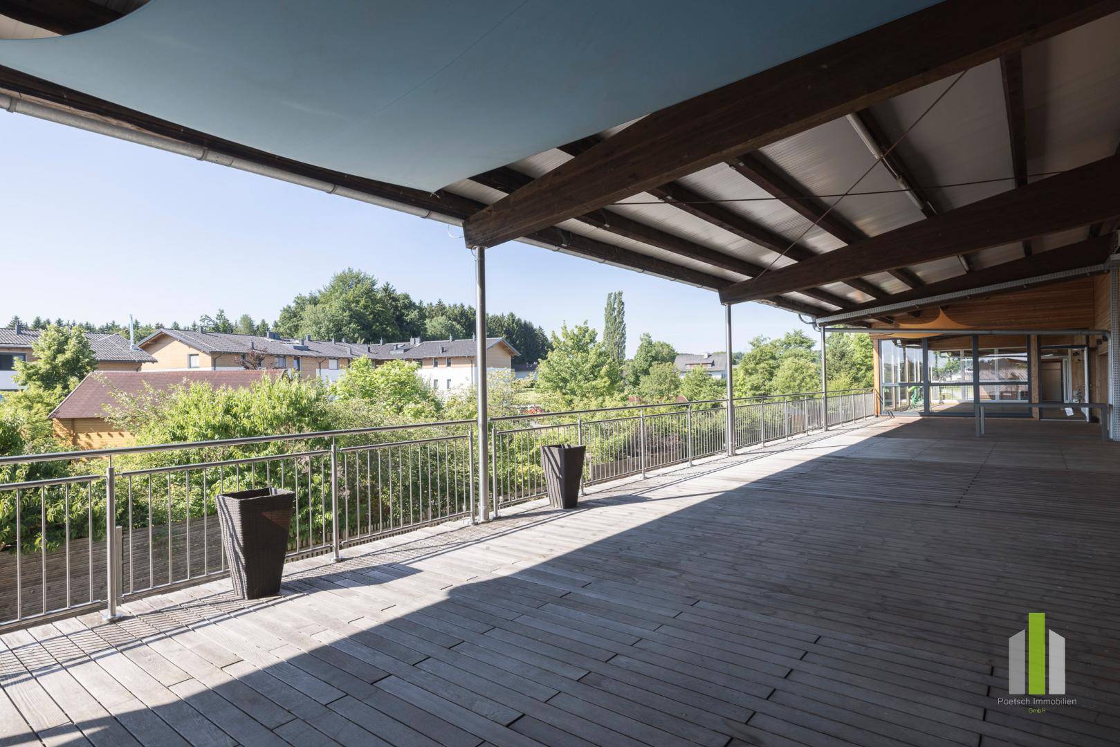 Weitläufige Holzterrasse mit Metallgeländer und Blick auf die umliegenden Gebäude und Bäume.