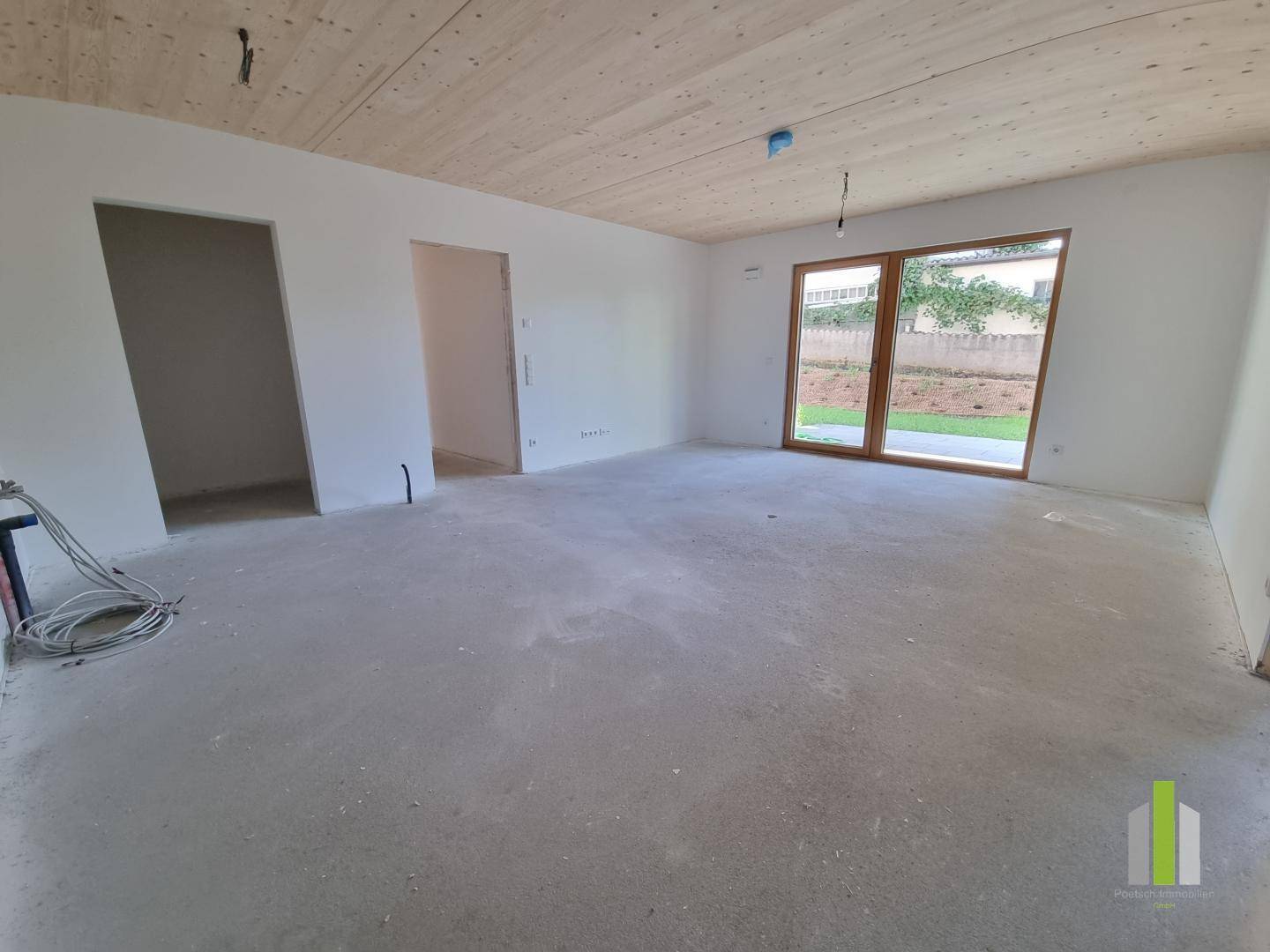 Heller, unmöblierter Wohnraum mit Holzbalkendecke und Zugang zu einem Außenbereich.