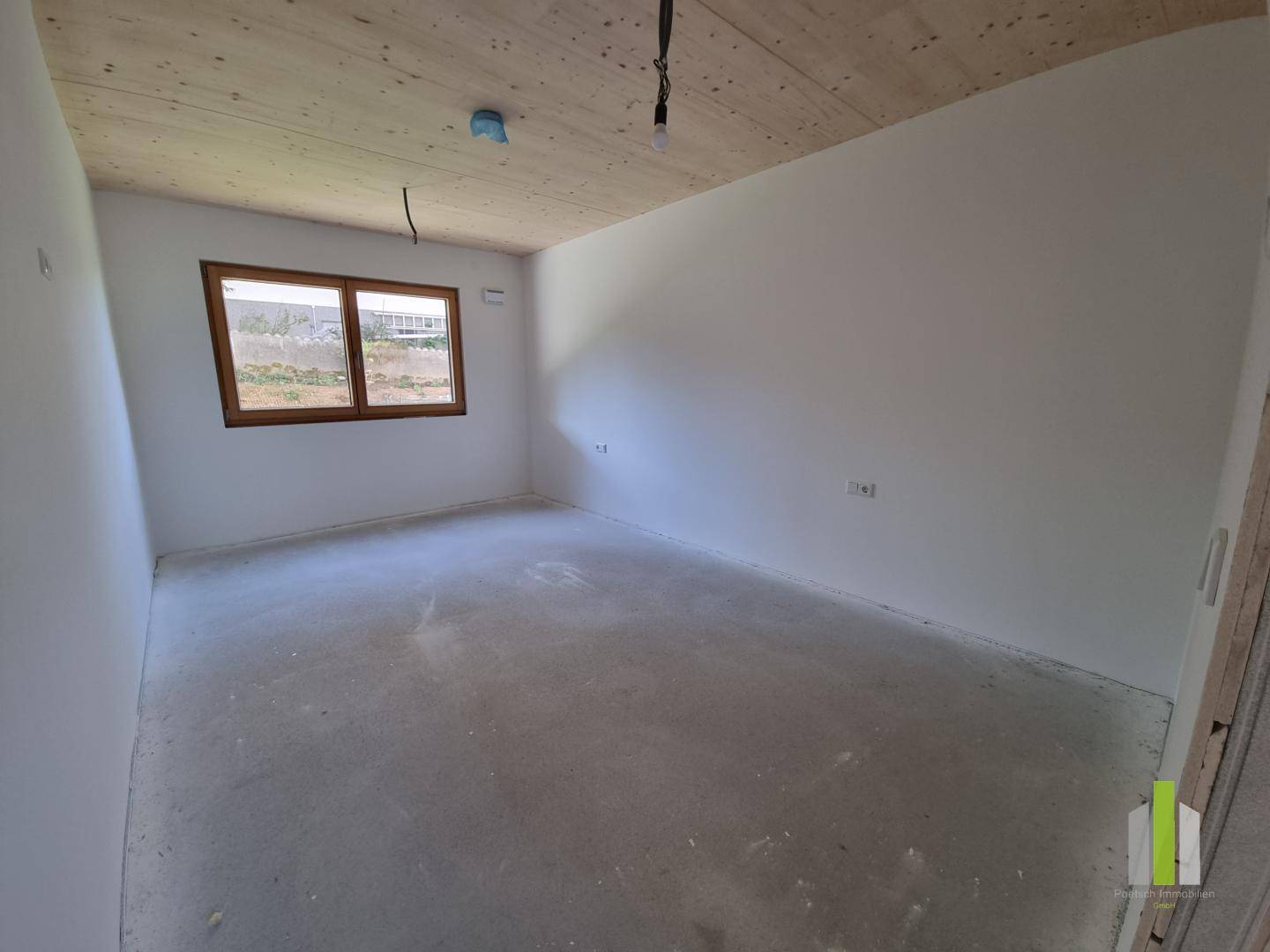 Unfertiges Schlafzimmer mit Holzbalkendecke, Betonboden und einem Fenster mit Blick ins Grüne.
