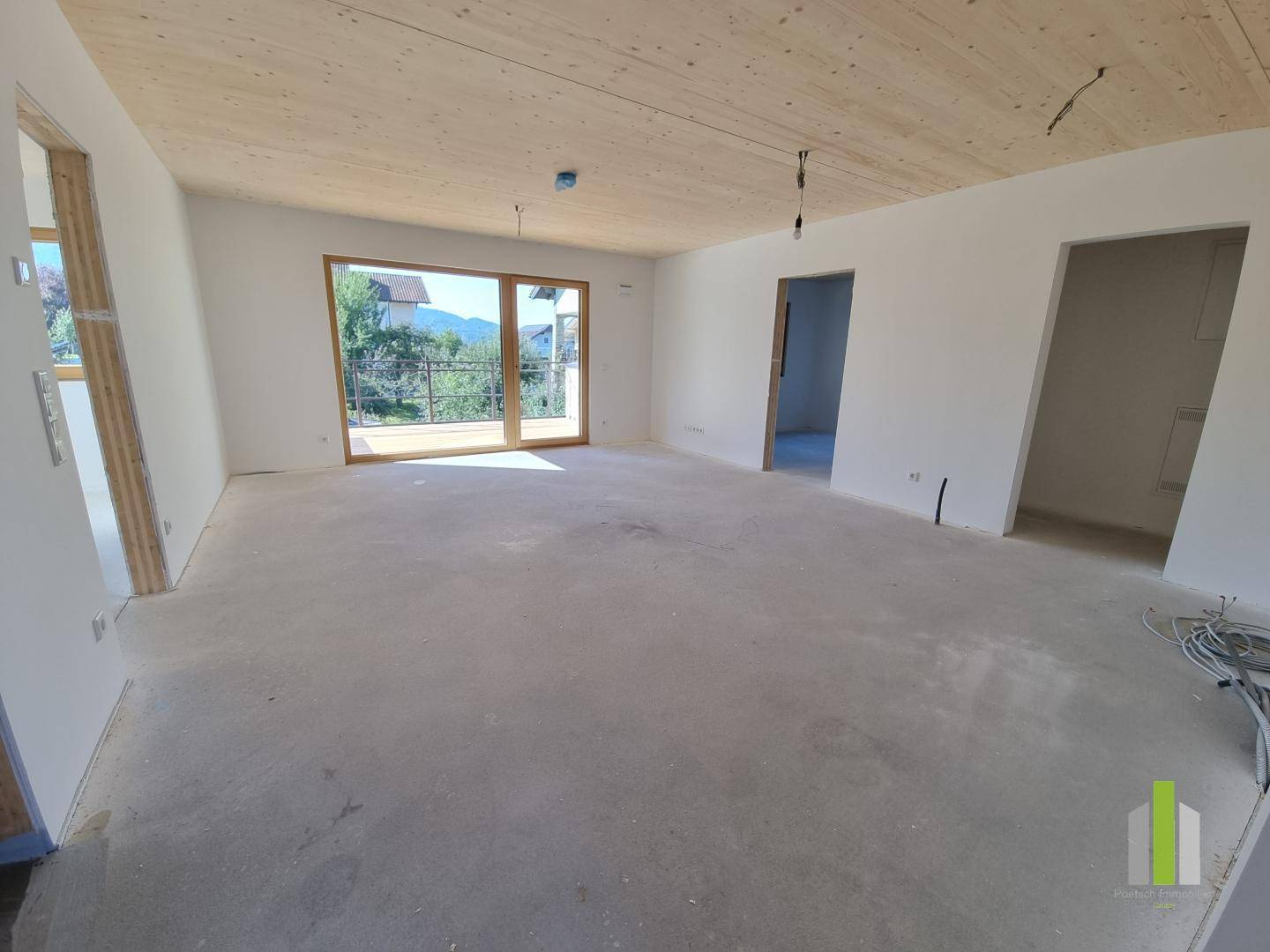 Großer, unfertiger Wohnbereich mit Holzbalkendecke und weitem Blick durch die Terrassentür.