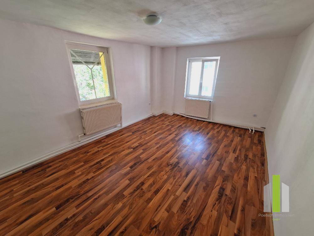 Schlafzimmer mit Holzboden, zwei Fenstern und Heizkörpern, gut beleuchtet.