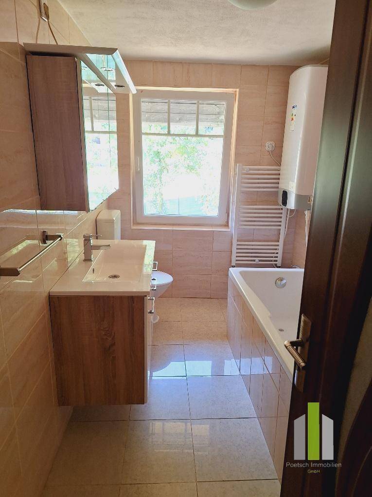 Badezimmer mit Badewanne, Waschbecken mit Unterschrank und Fenster.