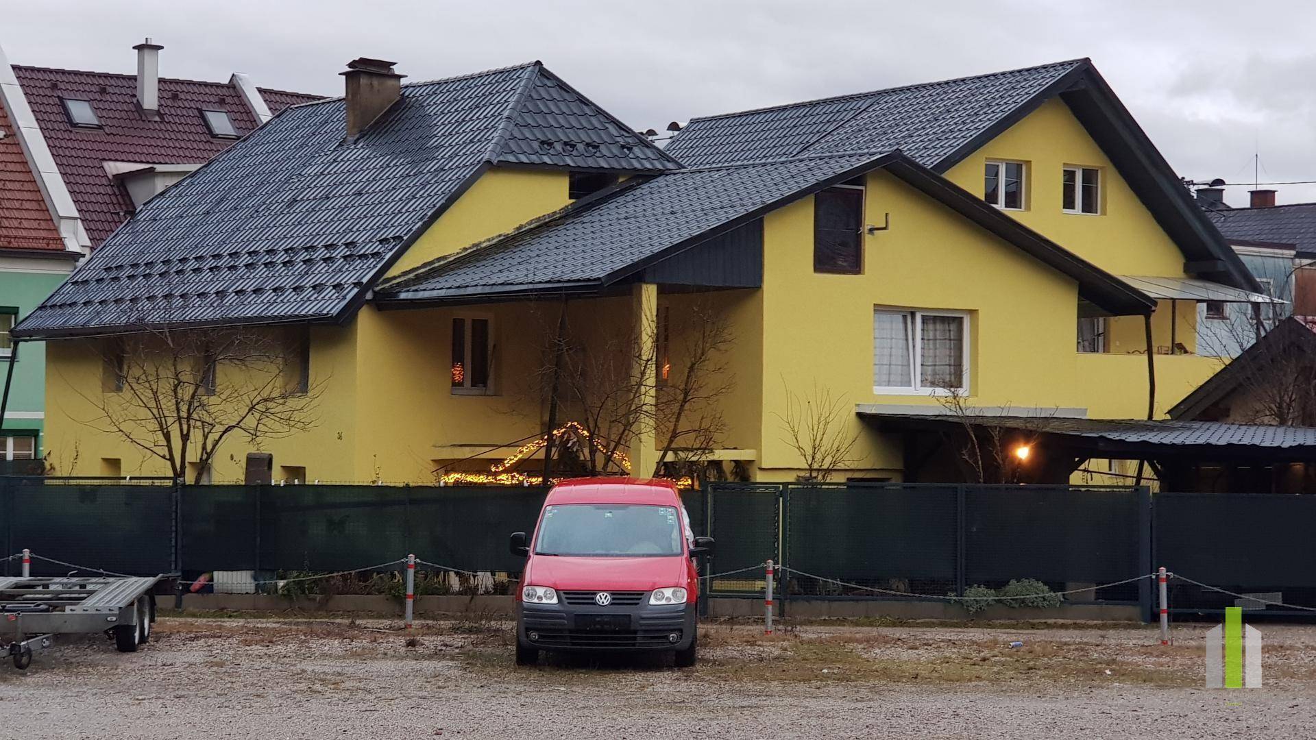 Gelbes Wohnhaus mit dunklem Ziegeldach und einem roten Lieferwagen davor.