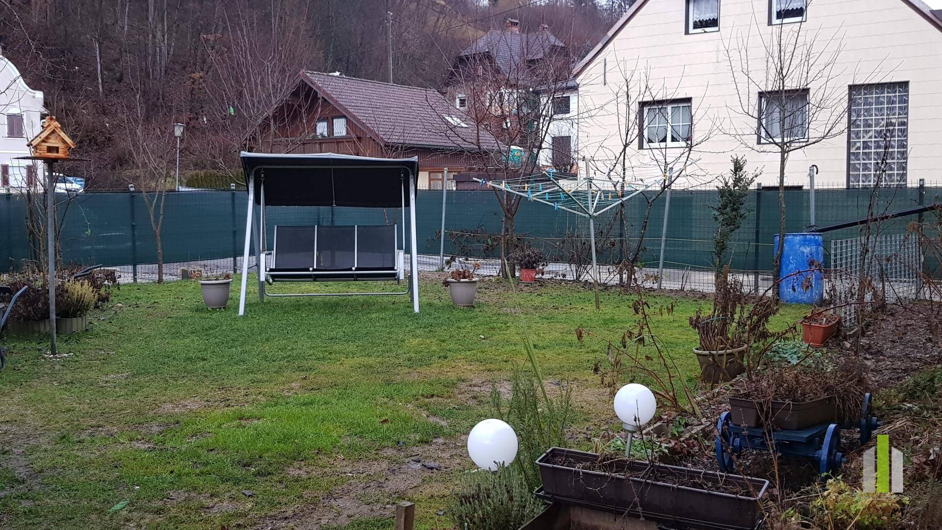 Grüner Gartenbereich mit Rasen, einer Gartenschaukel und verschiedenen Pflanzen.