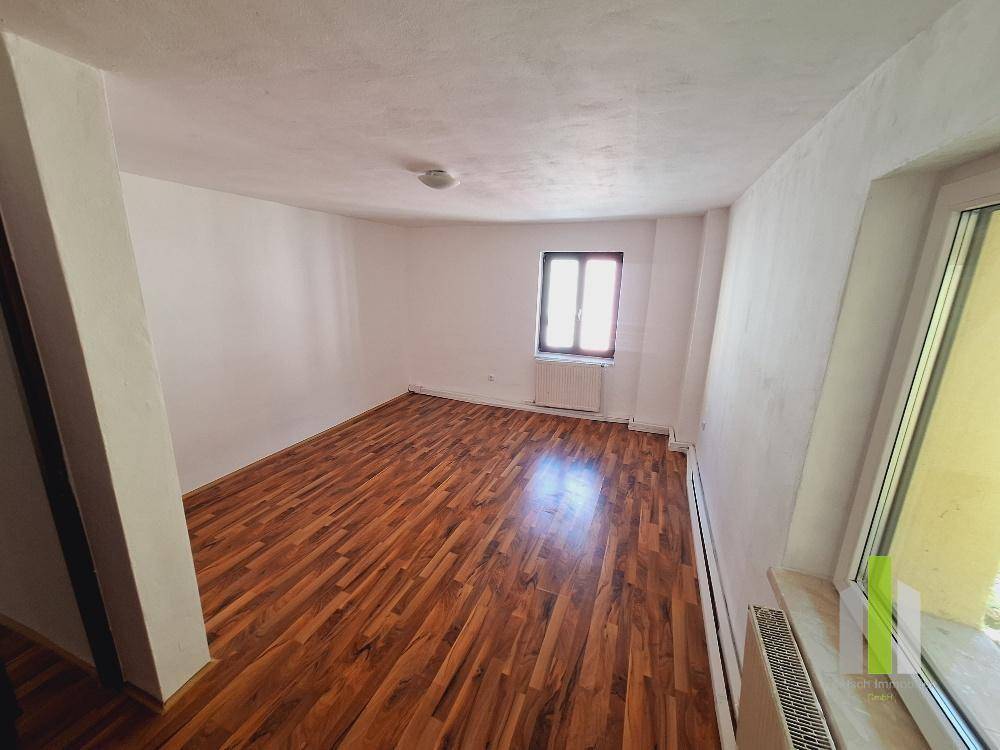 Helles Zimmer mit dunklem Parkettboden und Heizkörpern unter den Fenstern.