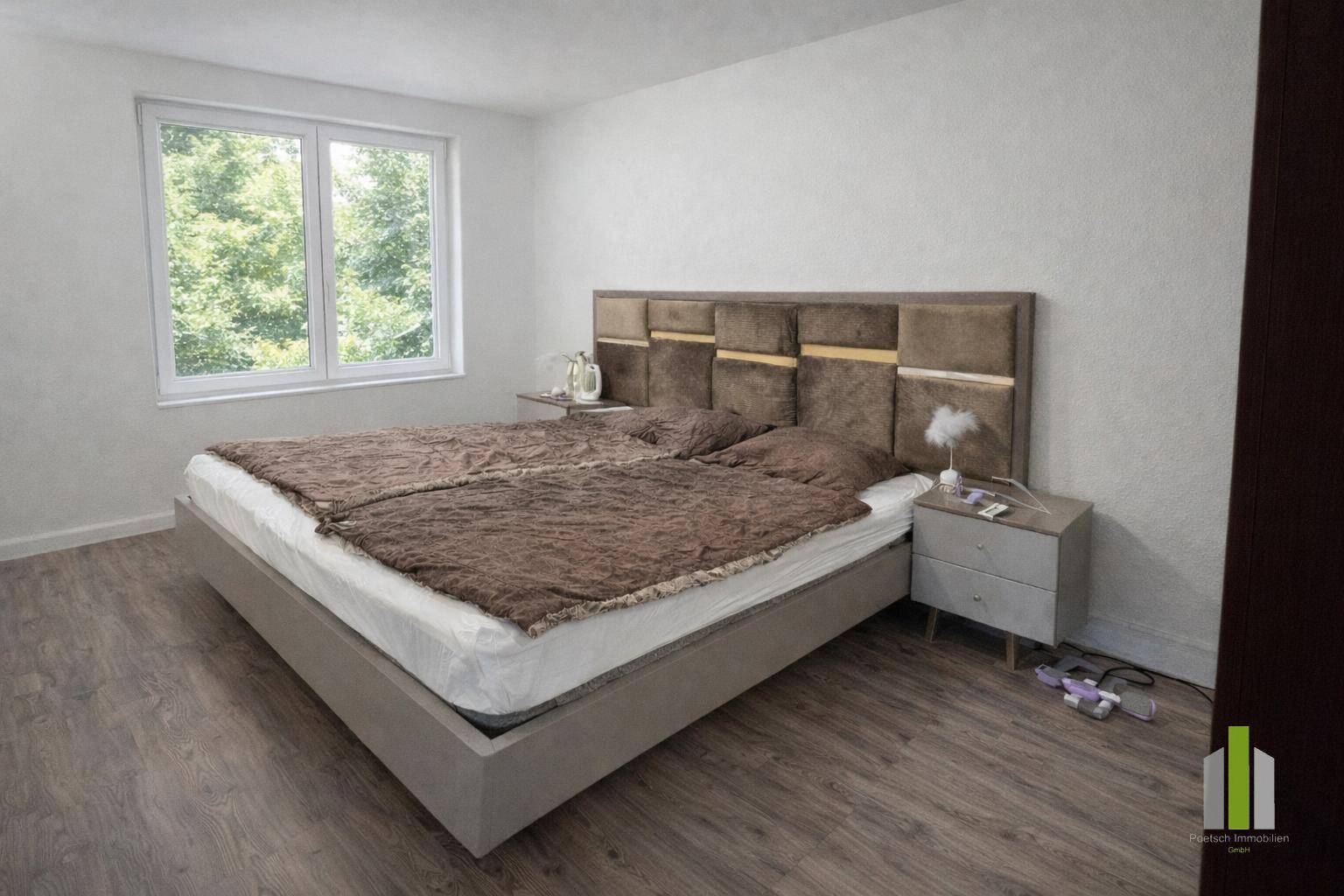 Modern eingerichtetes Schlafzimmer mit großem Bett, Laminatboden und hellem Fenster zum Garten.