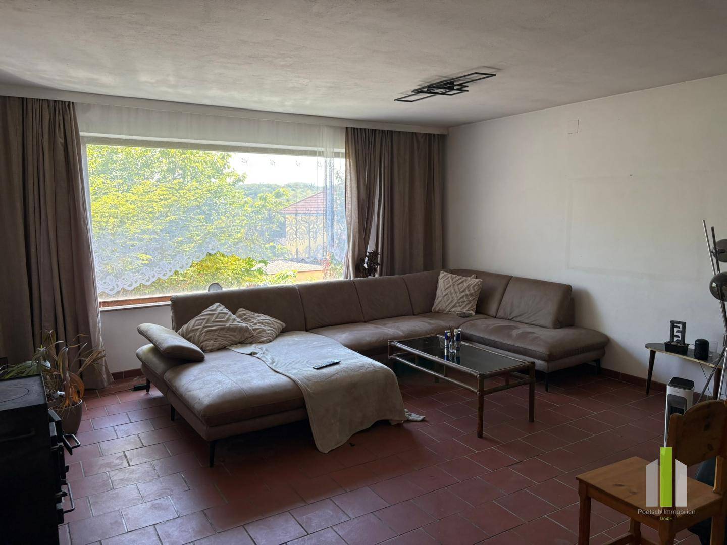 Helles Wohnzimmer mit großem Ecksofa, Terrakottafliesen und weitem Ausblick durch das breite Fenster.