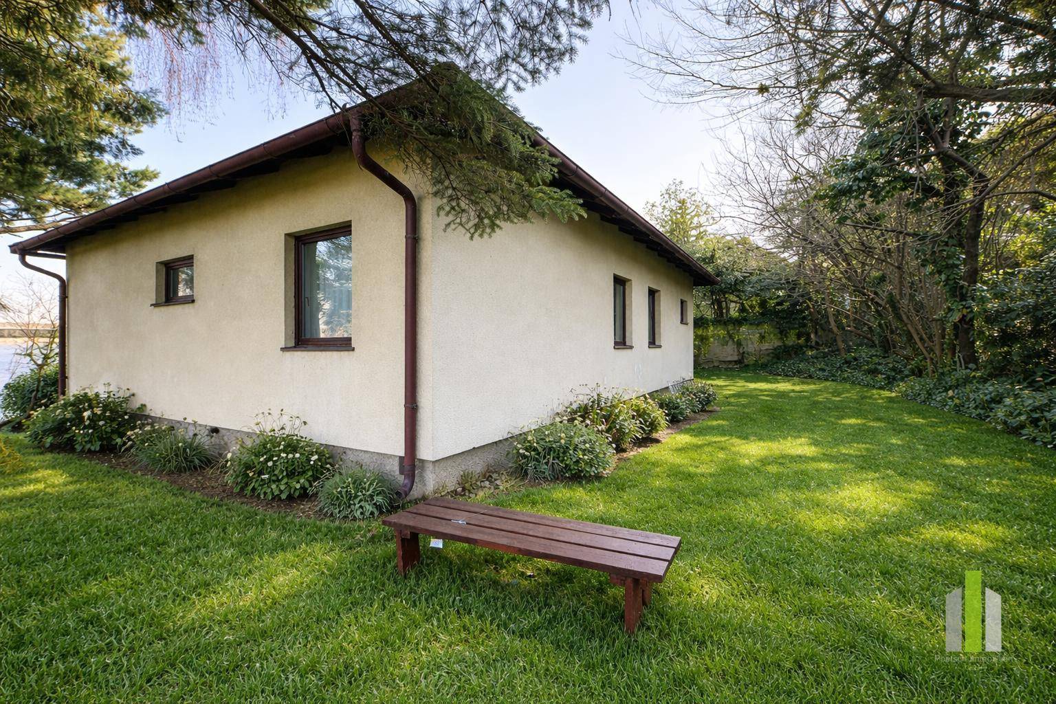 Weitläufiger Gartenbereich mit gepflegtem Rasen, Bäumen und einer Holzbank am Haus.