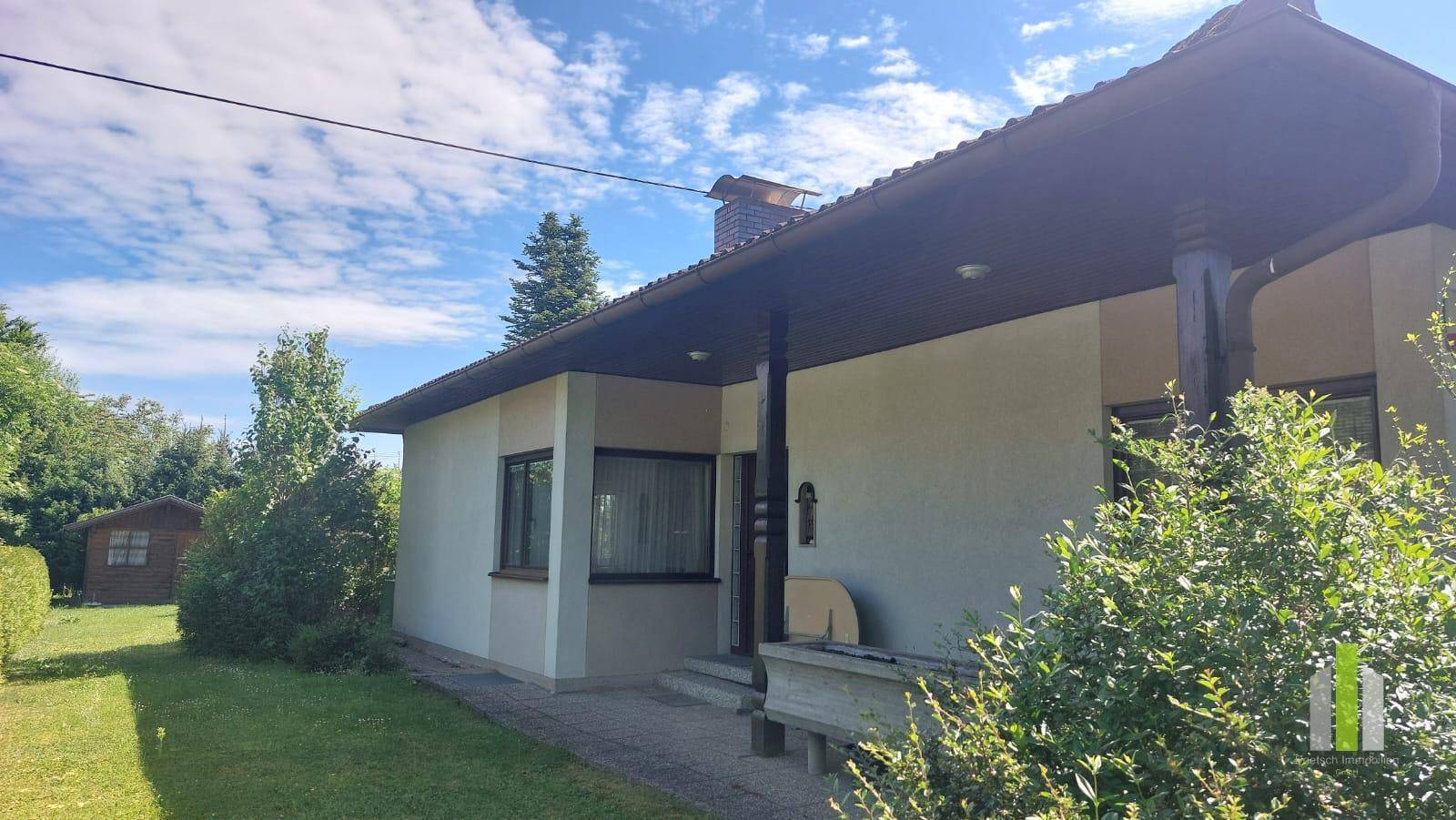 Ansicht des Hauses mit überdachtem Eingangsbereich und gepflegter Vorgartenlandschaft.