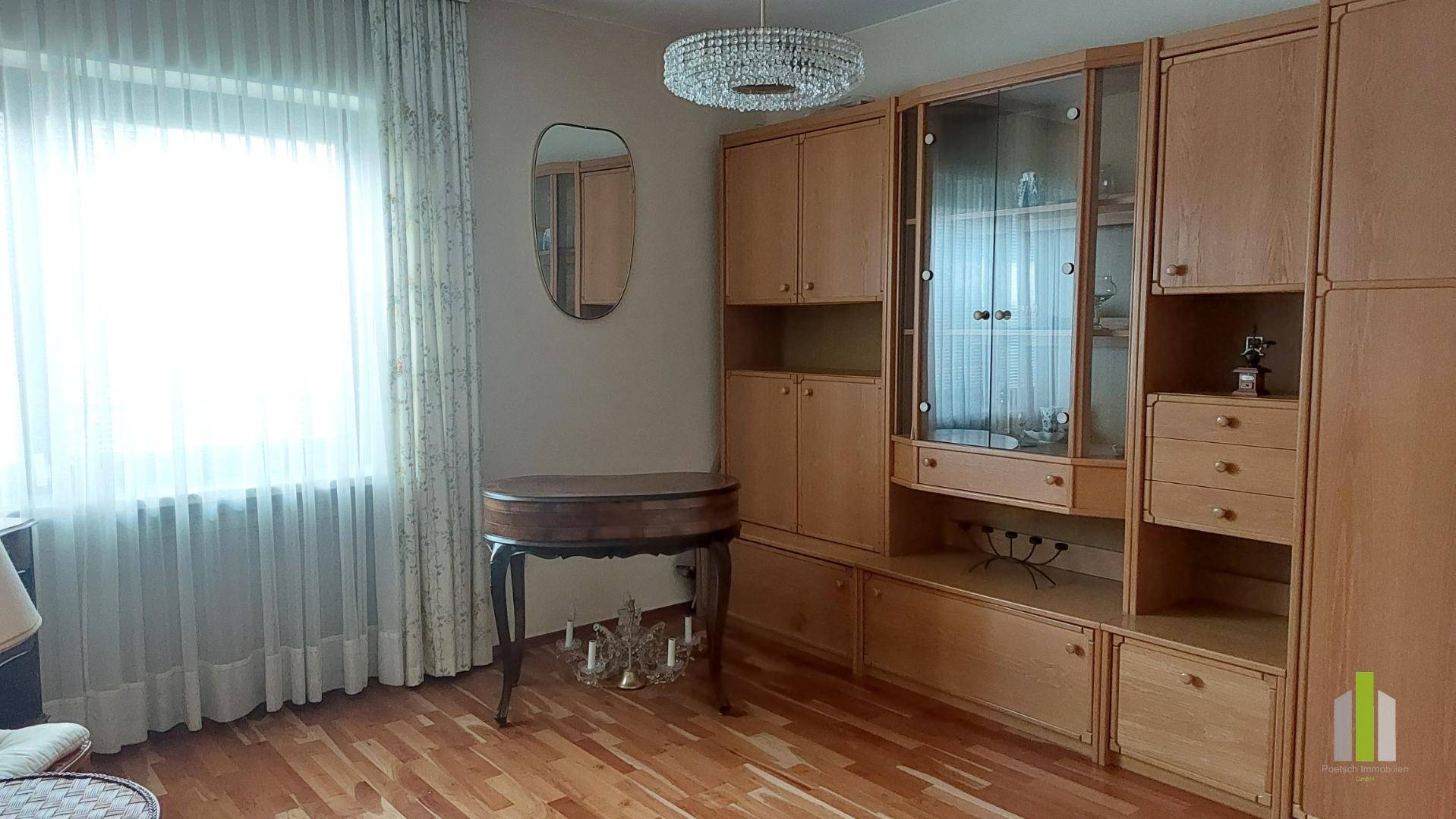 Wohnzimmer mit Parkettboden und einer großen Holzschrankwand, die viel Stauraum bietet.