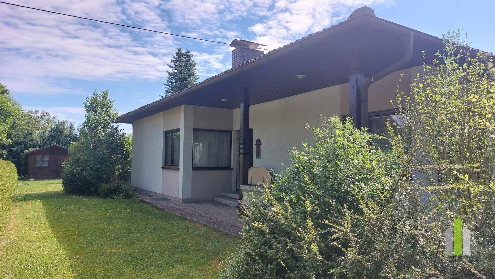 Ansicht des Hauses mit überdachtem Eingangsbereich und gepflegter Vorgartenlandschaft.