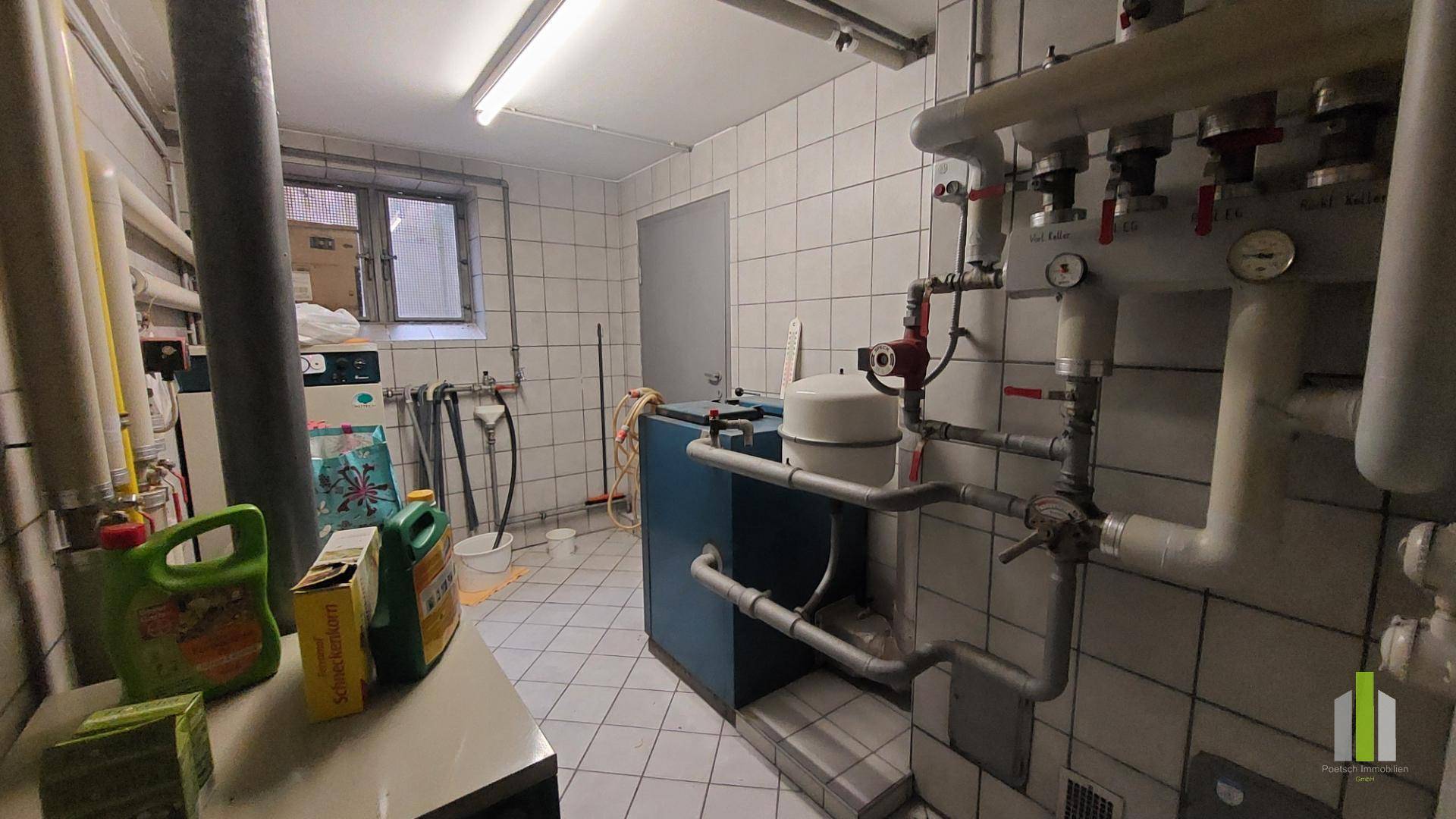 Technikraum im Untergeschoss mit Heizungsanlage, Leitungen und gefliesten Wänden.