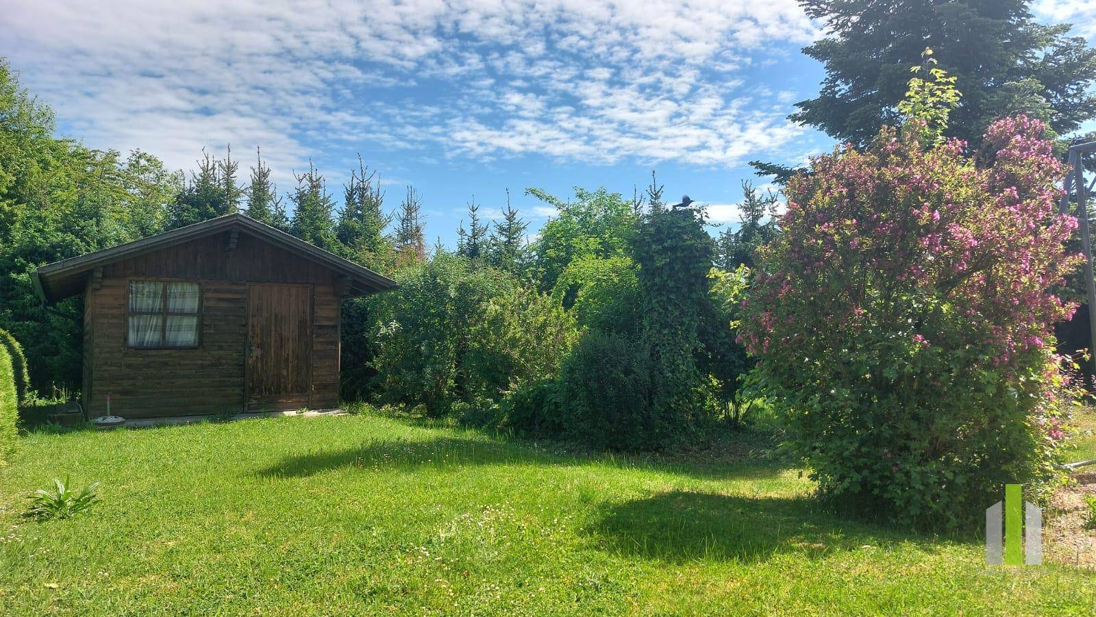 Geräumiger Garten mit einem charmanten Holzgartenhaus, umgeben von Bäumen und Sträuchern.