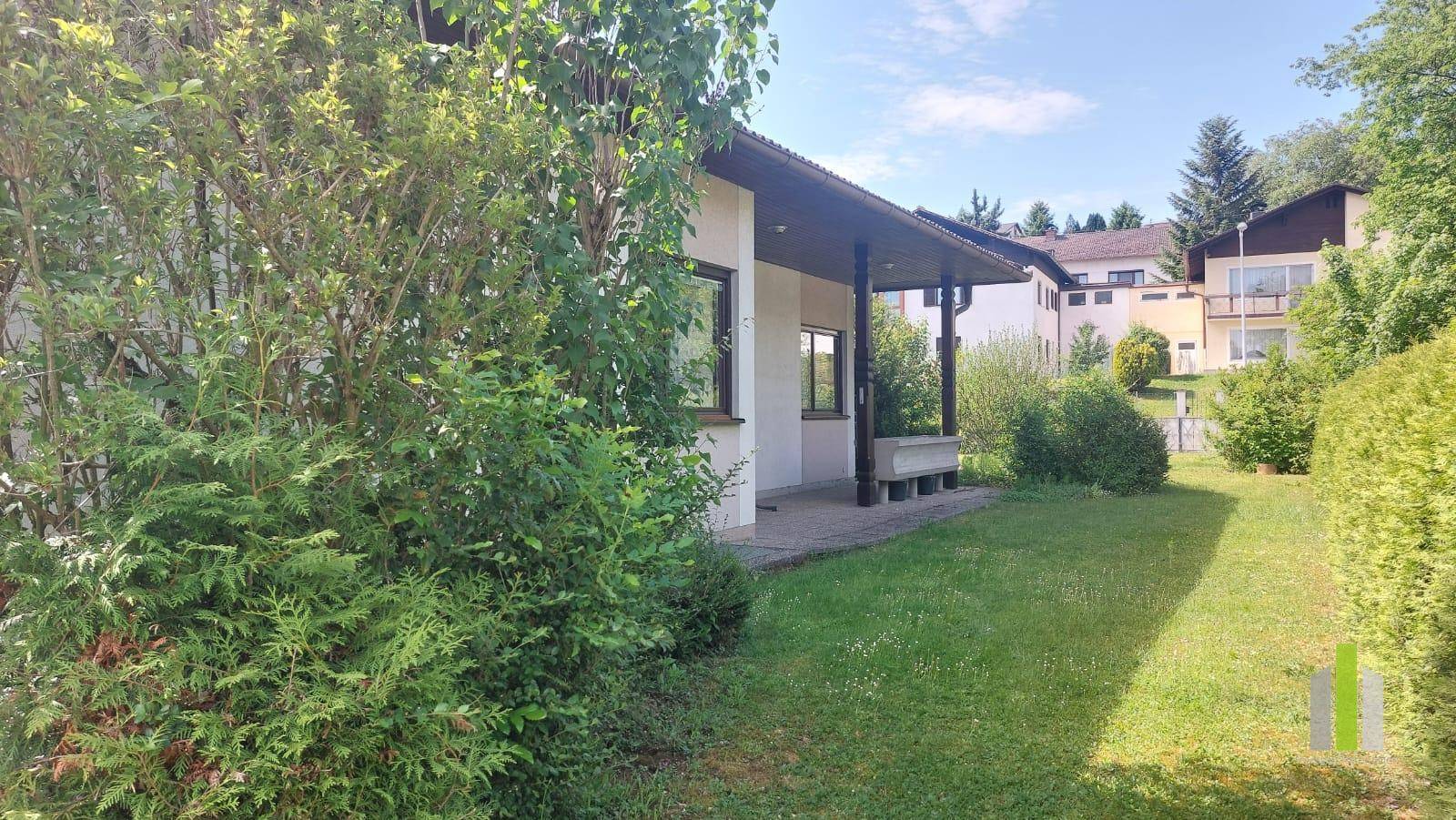Seitenansicht des Hauses mit überdachtem Bereich und weitläufigem Garten mit viel Grün.