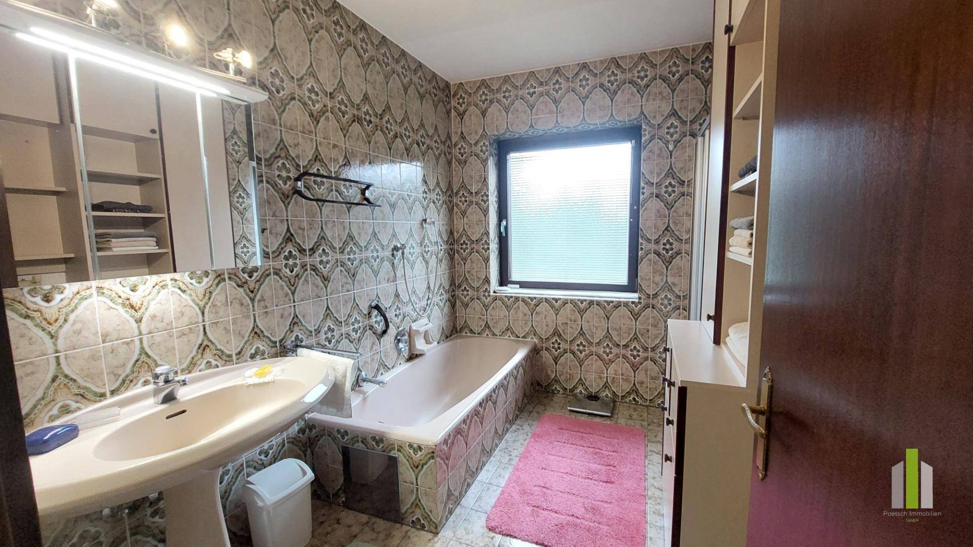Badezimmer mit Badewanne, Waschbecken und gemusterten Fliesen an Wänden und Boden.