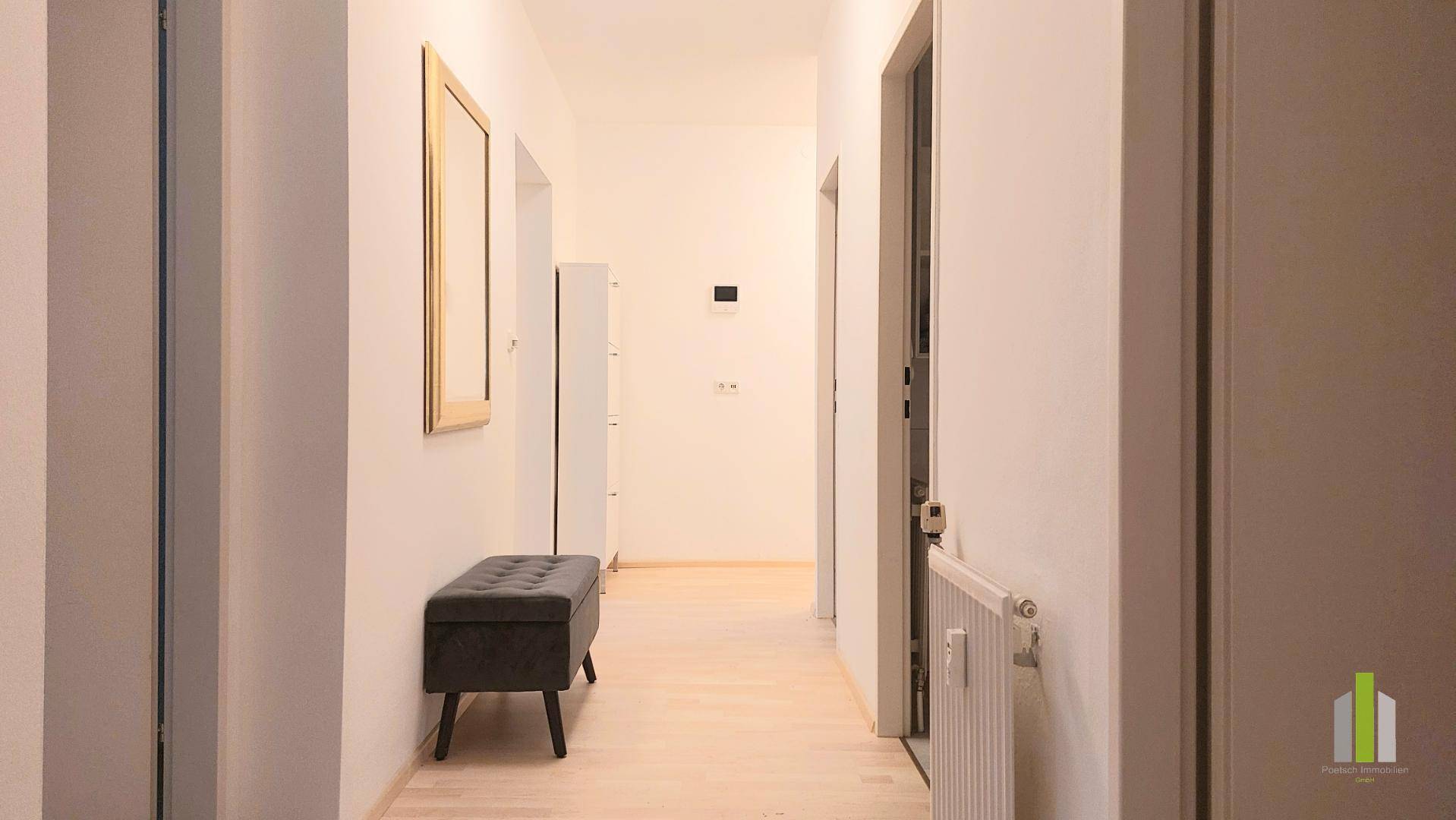 Heller Flur mit Holzboden, einer Sitzbank und einem großen Wandspiegel.