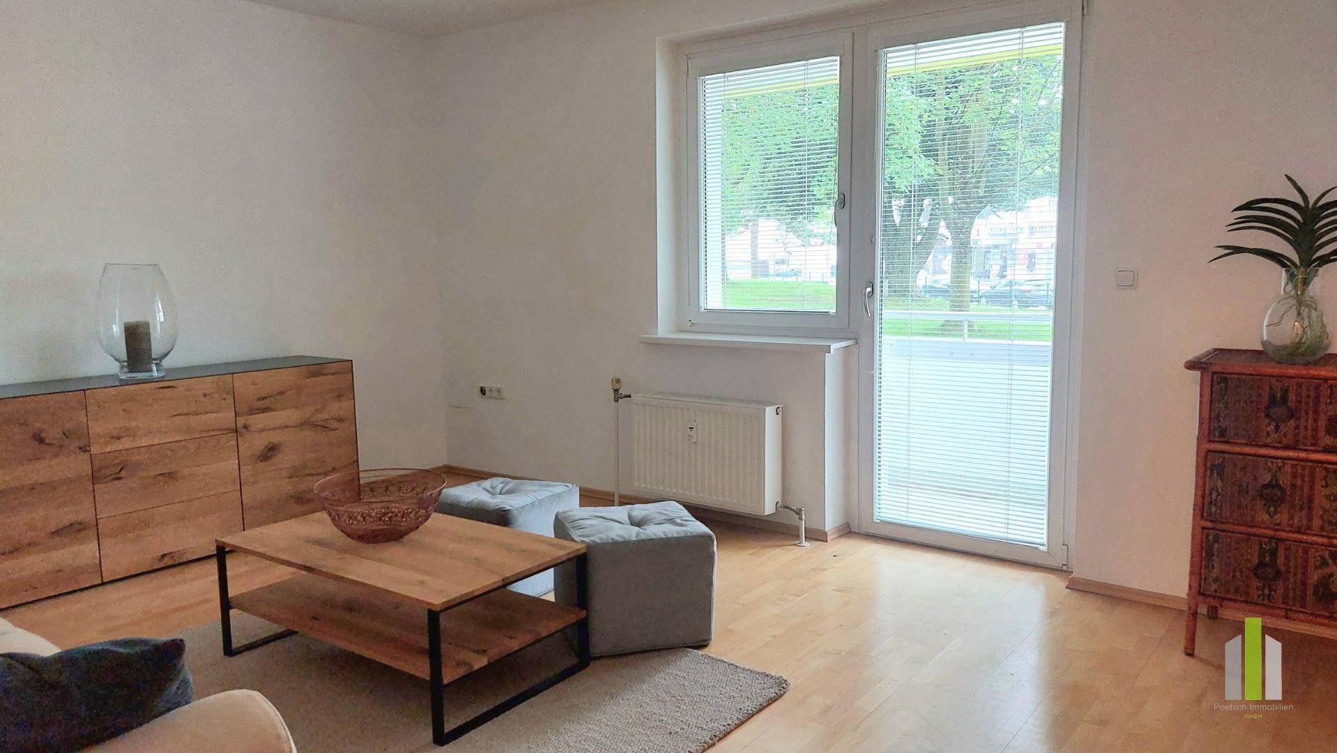Wohnzimmer mit Parkettboden und großem Fenster, das viel Tageslicht hereinlässt.