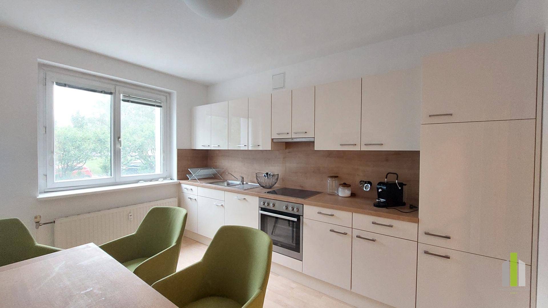 Moderne Einbauküche mit weißen Schränken, Holzarbeitsplatte und Essbereich am Fenster.