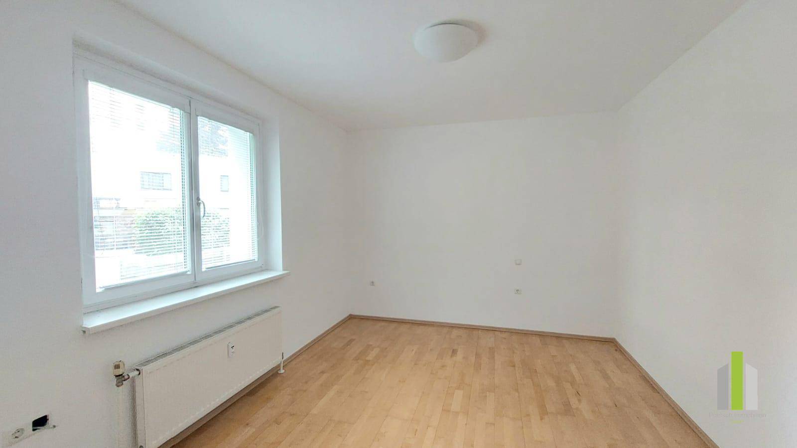 Leerer Raum mit Parkettboden und großem Fenster, ideal als Schlaf- oder Arbeitszimmer.