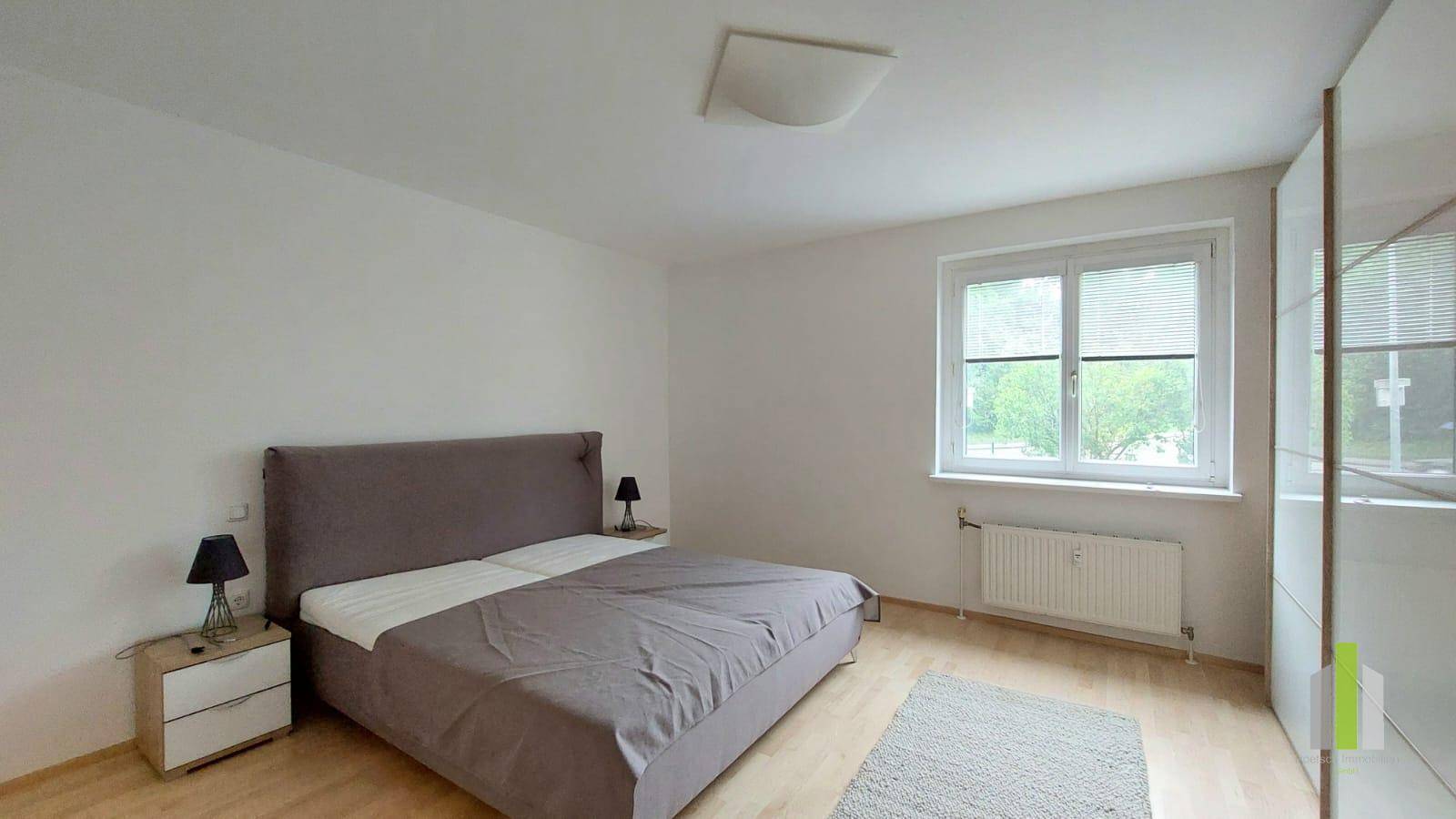 Schlafzimmer mit Doppelbett, Nachttischen und einem großen Fenster für viel Tageslicht.
