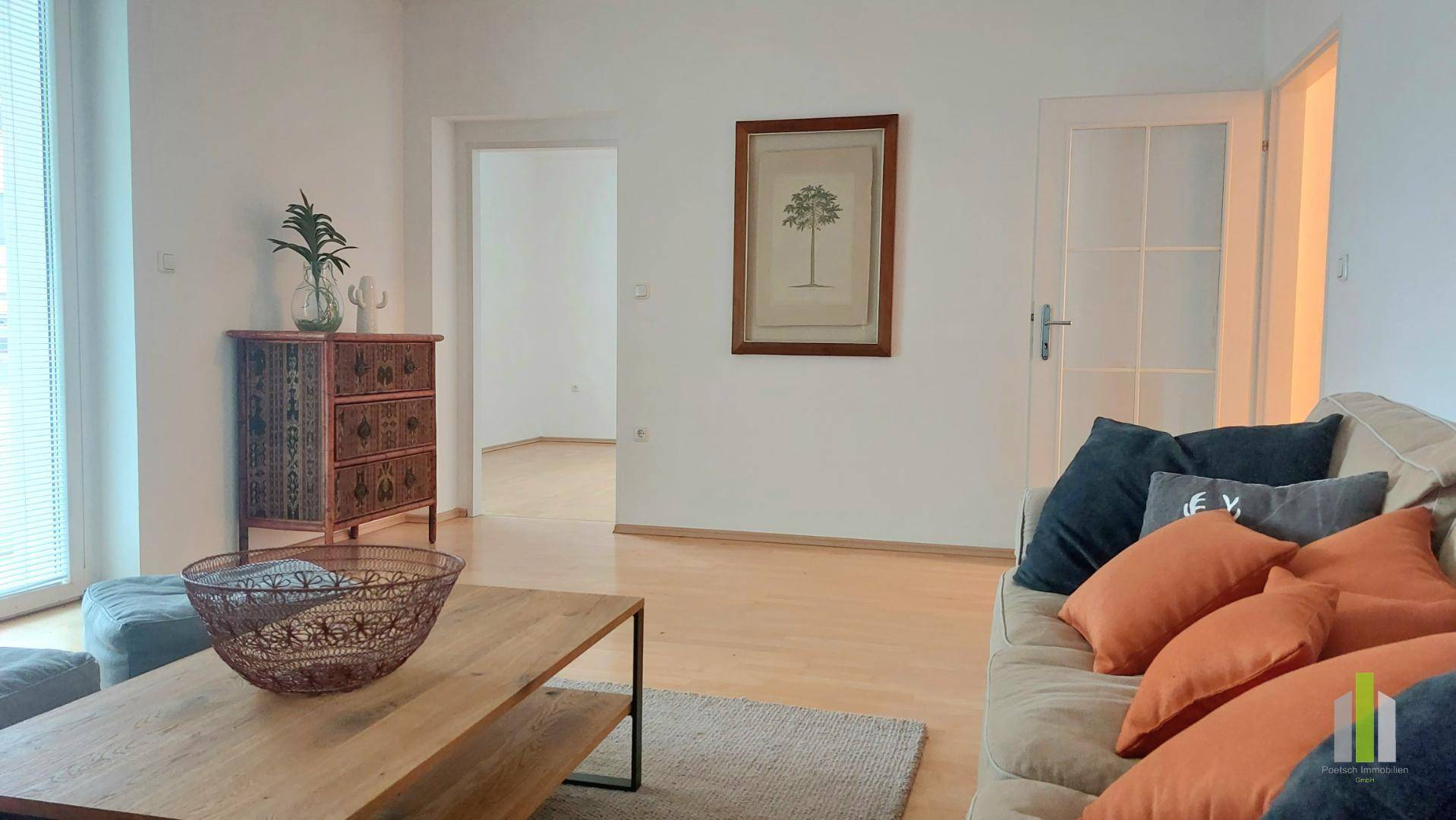 Gemütliches Wohnzimmer mit Holzboden, bequemer Couch und offenen Durchgängen zu angrenzenden Räumen.