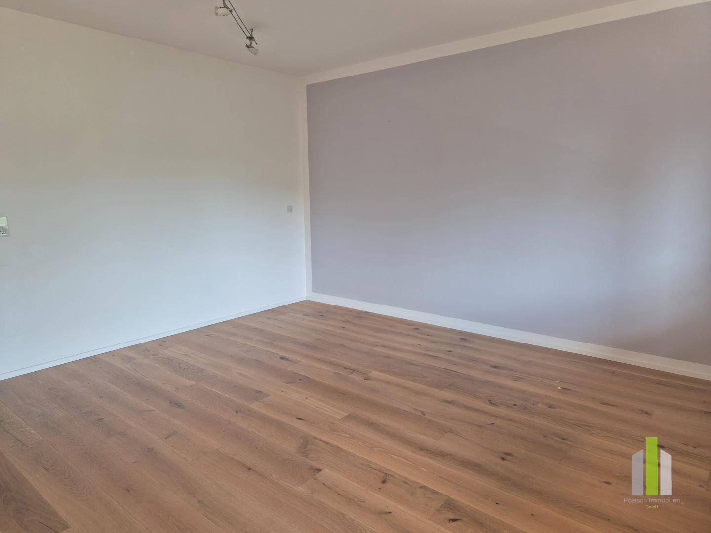 Heller Raum mit Holzboden und einer Akzentwand in sanftem Grau, bereit zur individuellen Gestaltung.