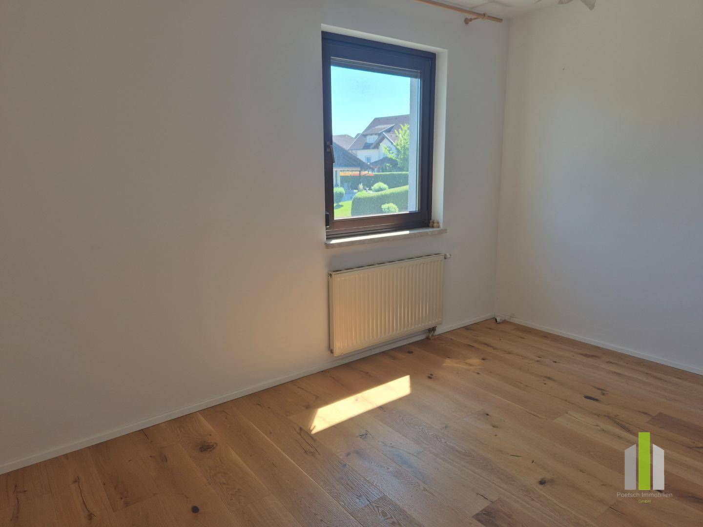 Ruhiges Zimmer mit Holzboden und Fenster, das einen Blick auf die Nachbarschaft bietet.