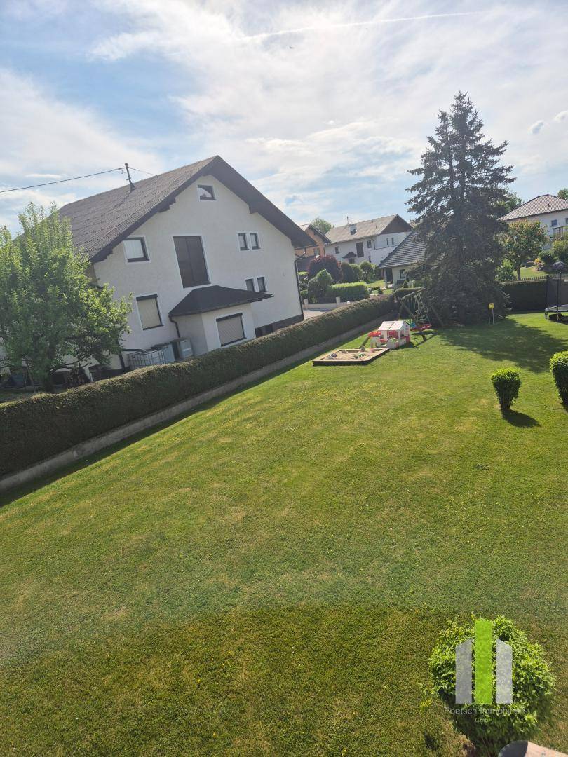 Großer, gepflegter Garten mit Rasenfläche, Hecke und Kinderspielplatz im Hintergrund.