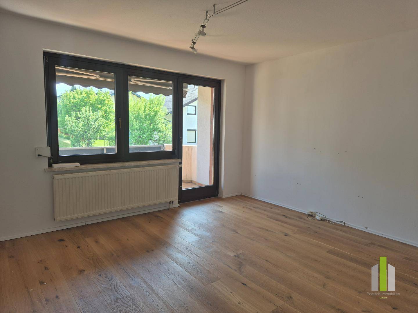 Geräumiges Zimmer mit Holzboden und großem Fenster, das viel Tageslicht hereinlässt.