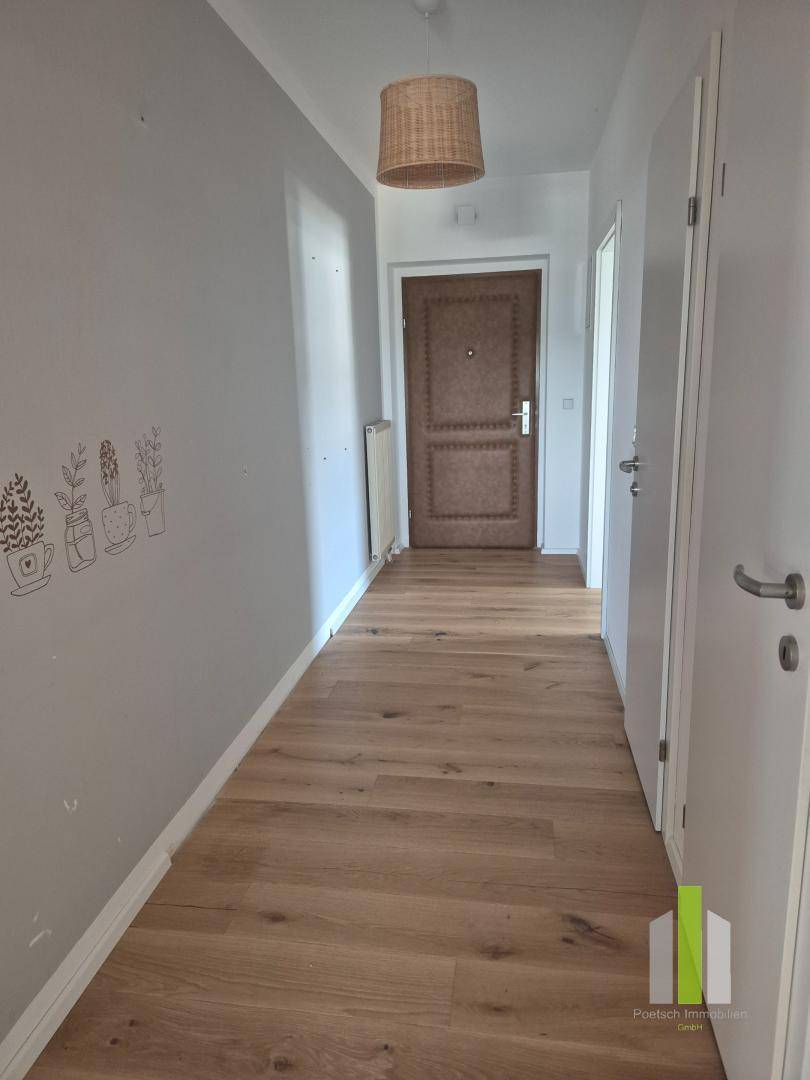 Heller Flur mit Holzboden und einer Eingangstür, die den Zugang zur Wohnung ermöglicht.