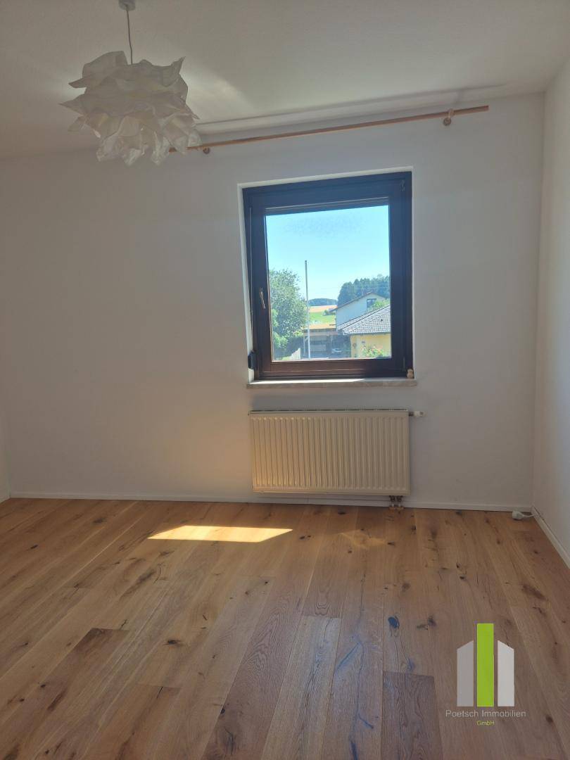 Helles Schlafzimmer mit Holzboden und einem Fenster, das viel Sonnenlicht hereinlässt.