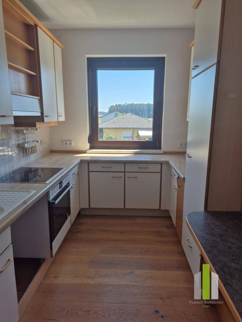 Funktionale Küche mit Holzboden, Einbauschränken und Fenster mit Blick ins Grüne.