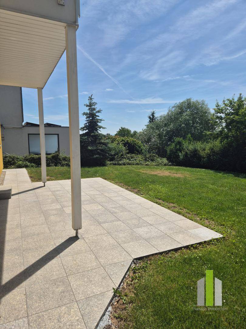 Große gepflasterte Terrasse mit Blick auf den weitläufigen, grünen Gartenbereich des Hauses.