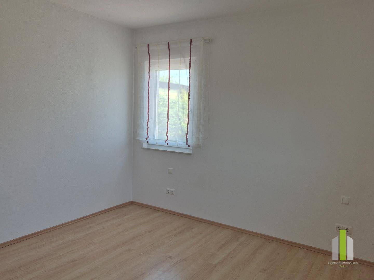 Heller, leerer Raum mit Laminatboden und einem Fenster, bietet eine neutrale Basis für individuelle Gestaltung.