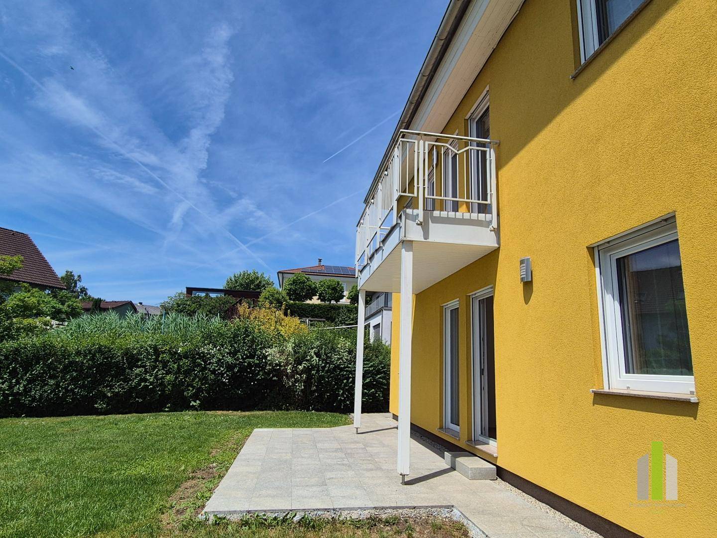 Seitenansicht des Hauses mit Balkon, gepflasterter Terrasse und einem gepflegten Gartenbereich.