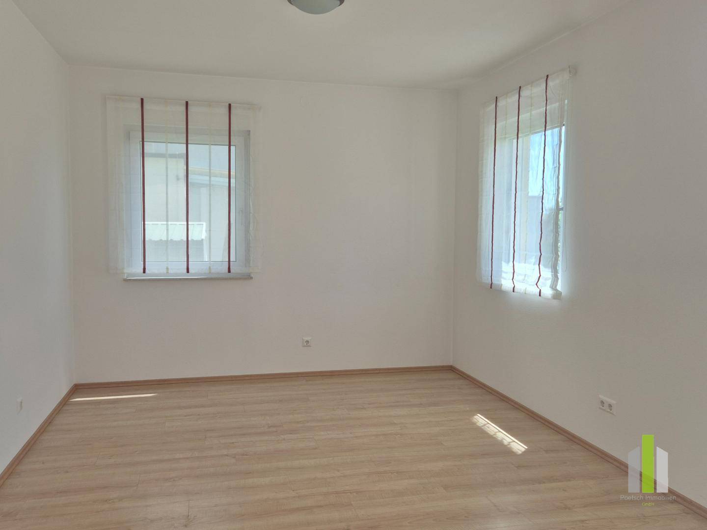 Leerer Raum mit Laminatboden und zwei Fenstern, bietet viel Tageslicht und flexible Nutzungsmöglichkeiten.