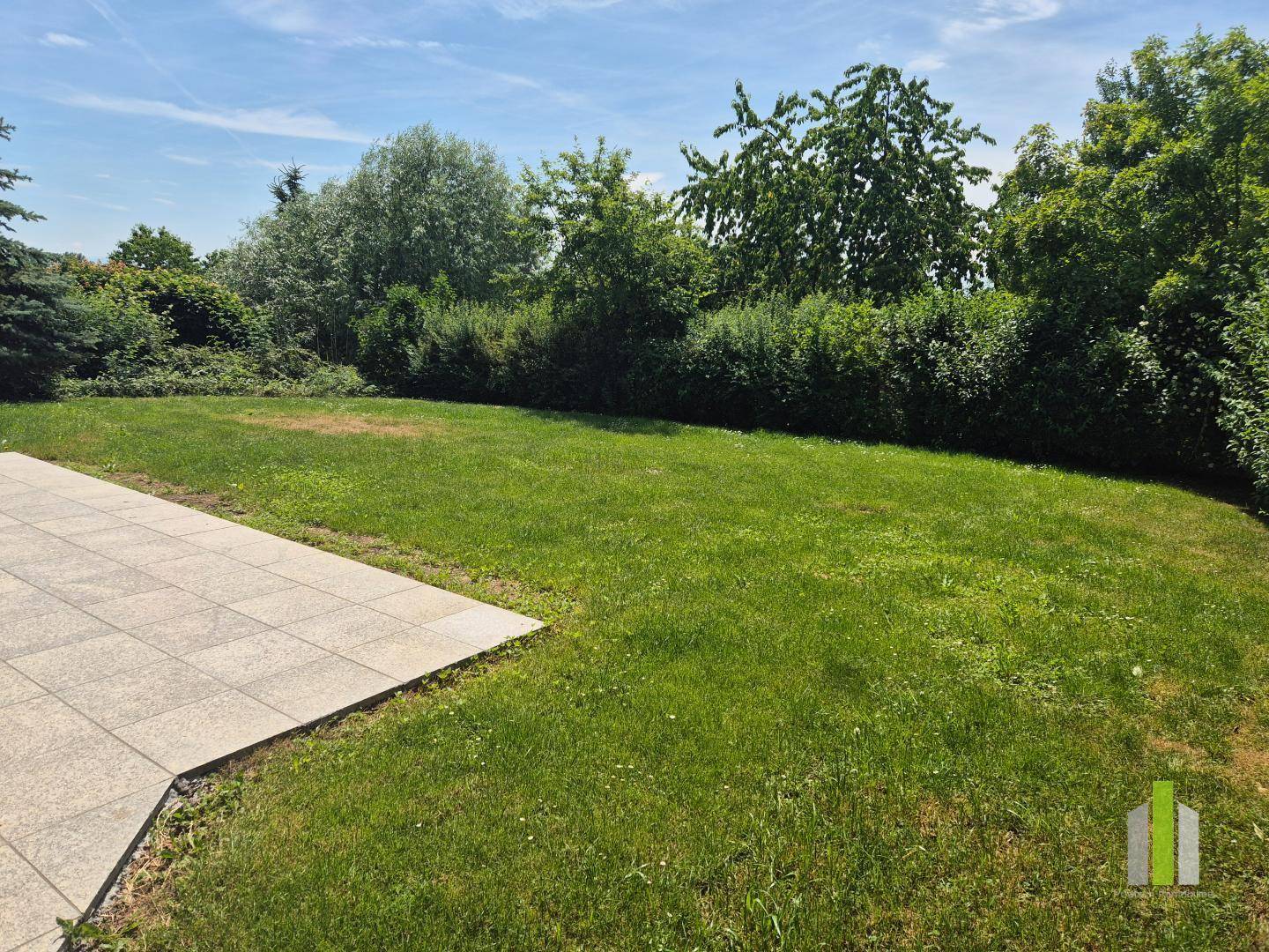 Sonniger Garten mit großer Rasenfläche und Blick auf die umliegende grüne Landschaft.