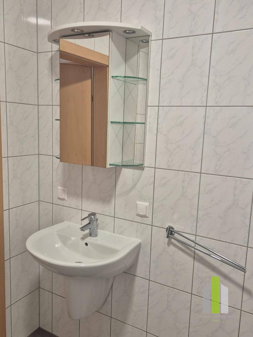 Badezimmer mit Waschbecken und Spiegelschrank, hell gefliesten Wänden und dunklem Boden, praktisch eingerichtet.