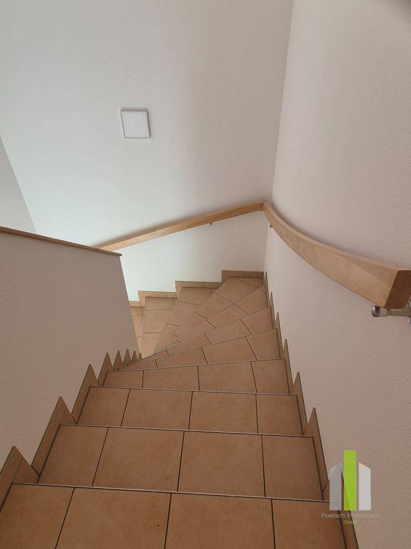 Treppenhaus mit gefliesten Stufen und einem eleganten Holzhandlauf, führt in die oberen Etagen.