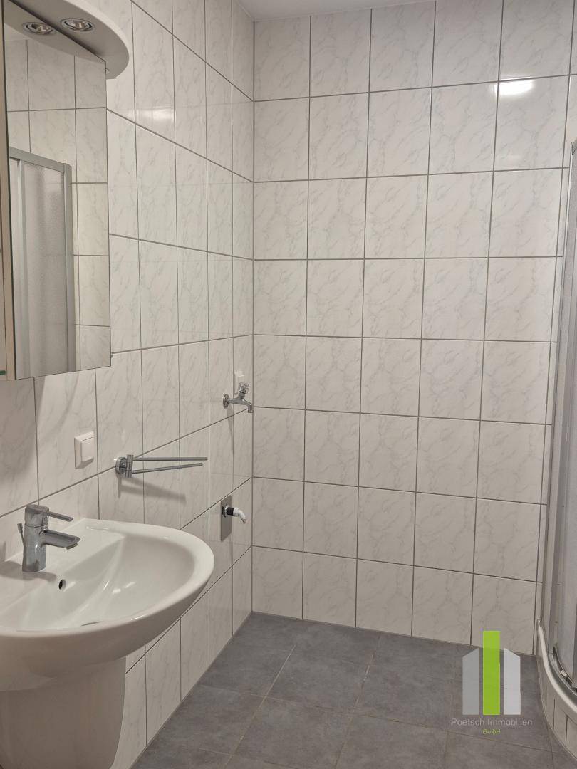 Helles Badezimmer mit Waschbecken, Spiegelschrank und Duschbereich, komplett gefliest für einfache Pflege.